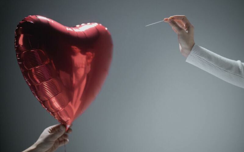 Roter Herzballon wird mit Nadel zum Platzen gebracht